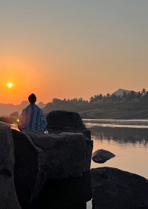 Frau-sitzt-bei-Sonnenaufgang-am-Fluss-in-Hampi