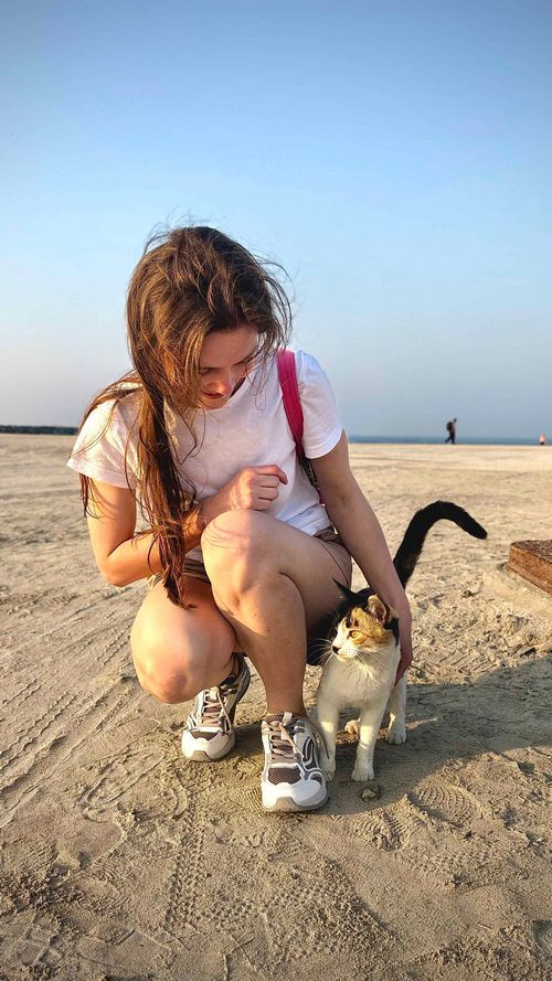junge Frau streichelt am Strand eine Katze